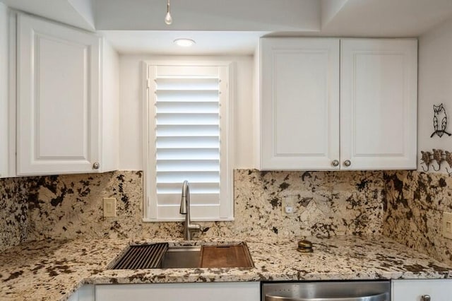 kitchen featuring tasteful backsplash, stainless steel dishwasher, a sink, and white cabinets