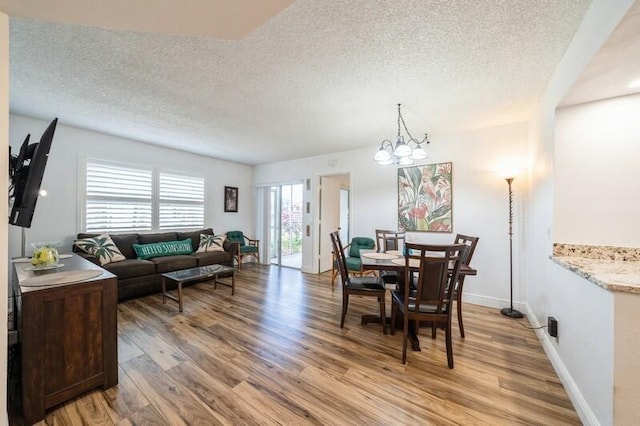 dining area with a notable chandelier, a textured ceiling, baseboards, and light wood-style floors