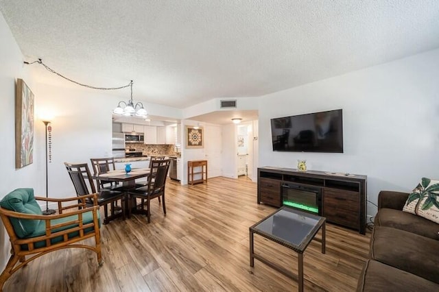 living area with visible vents, light wood-style flooring, a textured ceiling, and an inviting chandelier