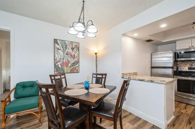 dining area featuring baseboards, a textured ceiling, light wood-style floors, a chandelier, and recessed lighting