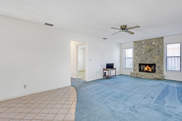 unfurnished living room with a wealth of natural light, visible vents, light colored carpet, and a stone fireplace