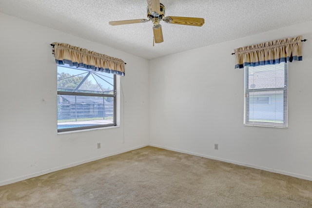 spare room featuring a wealth of natural light, light colored carpet, a textured ceiling, and a ceiling fan