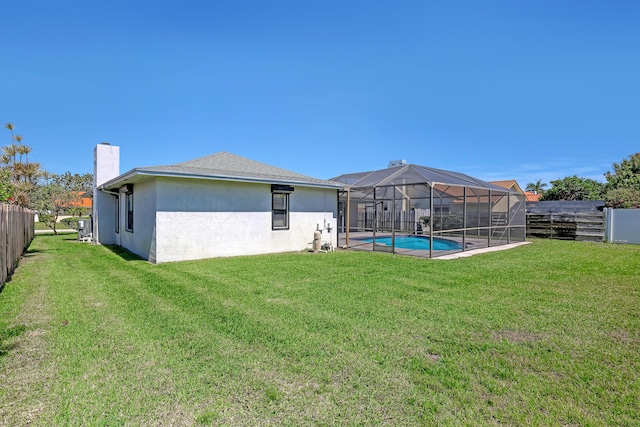 back of house with a yard, a fenced backyard, a chimney, stucco siding, and a lanai