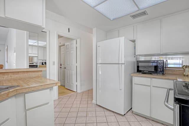 kitchen featuring visible vents, oven, black microwave, electric stove, and freestanding refrigerator