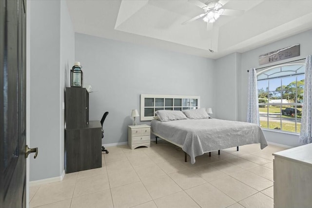 bedroom with light tile patterned floors, baseboards, a tray ceiling, and a ceiling fan