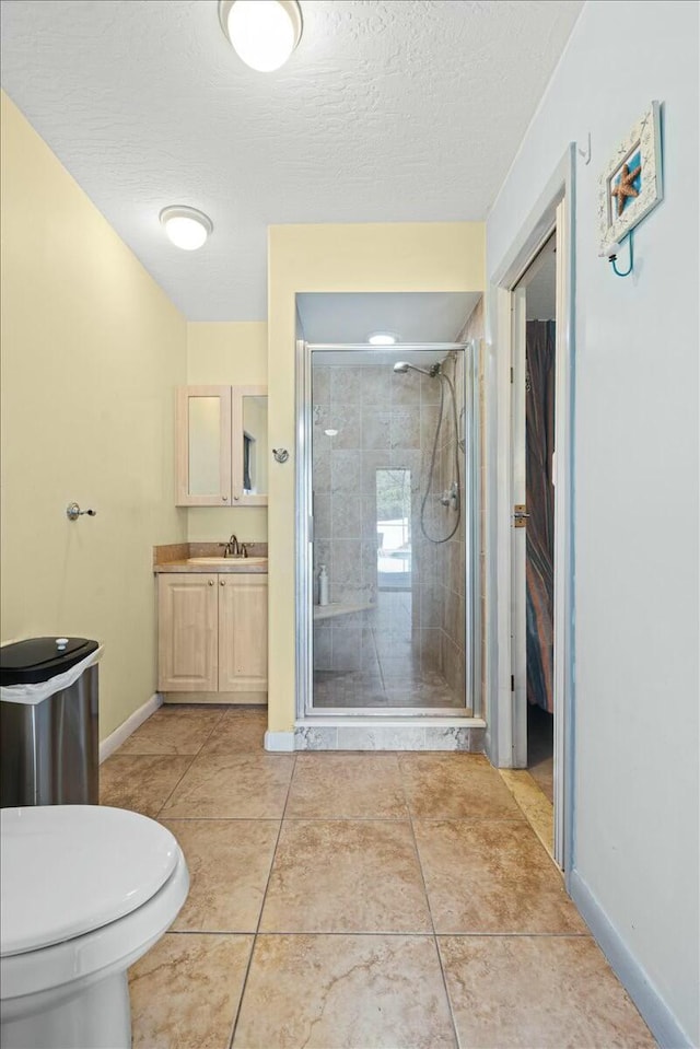 full bathroom featuring a stall shower, vanity, a textured ceiling, tile patterned flooring, and baseboards