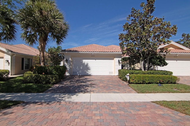 mediterranean / spanish house featuring a garage, a tiled roof, decorative driveway, and stucco siding