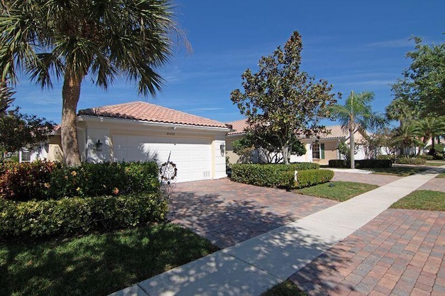 mediterranean / spanish-style house featuring an attached garage, a tile roof, decorative driveway, and stucco siding