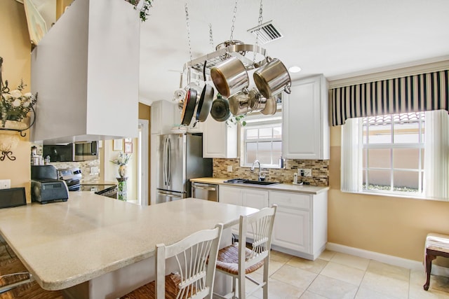 kitchen featuring a peninsula, a breakfast bar, a sink, appliances with stainless steel finishes, and decorative backsplash