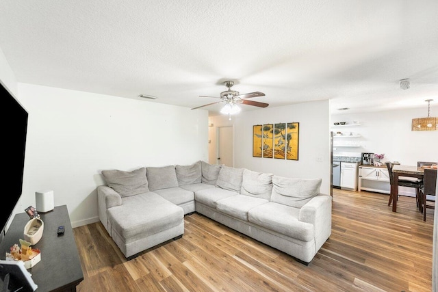 living room with visible vents, ceiling fan, light wood-style flooring, and a textured ceiling