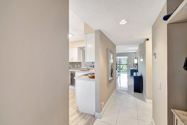 hallway featuring light wood-style floors, a sink, a textured ceiling, and baseboards