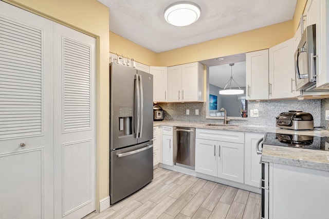 kitchen featuring white cabinets, appliances with stainless steel finishes, decorative backsplash, and a sink