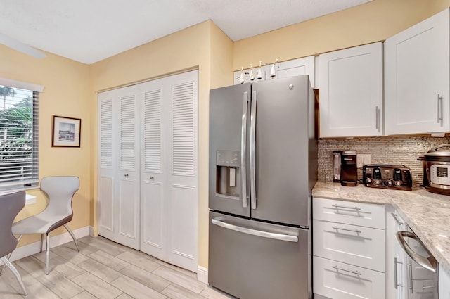 kitchen with stainless steel fridge, baseboards, white cabinets, decorative backsplash, and light stone counters