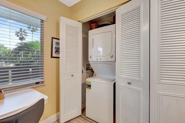 laundry area with light wood-type flooring, laundry area, baseboards, and stacked washer / dryer