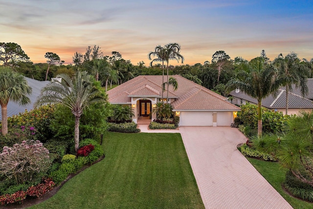 mediterranean / spanish-style house with decorative driveway, a tile roof, stucco siding, a garage, and a front lawn