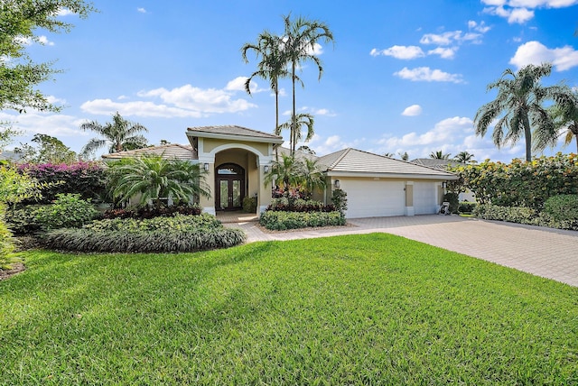 mediterranean / spanish-style house with a garage, decorative driveway, french doors, a front lawn, and stucco siding