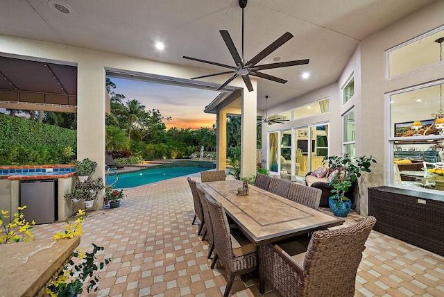 patio terrace at dusk featuring outdoor dining area, an outdoor pool, and ceiling fan