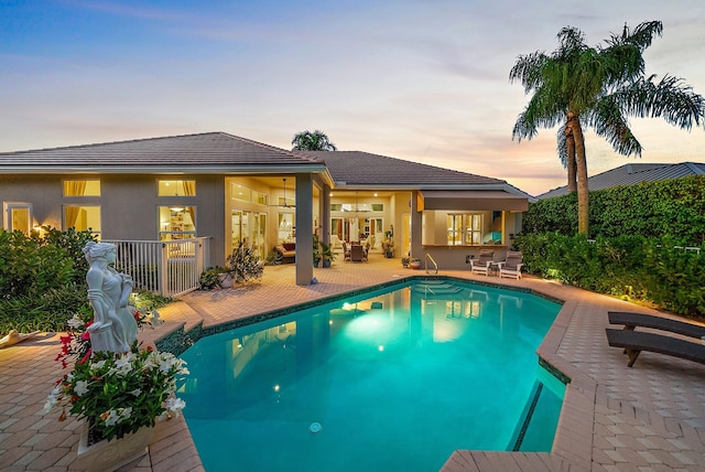 pool at dusk with a patio area and an outdoor pool