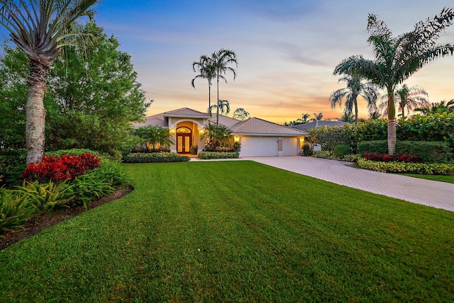 mediterranean / spanish house featuring a yard, decorative driveway, an attached garage, and stucco siding