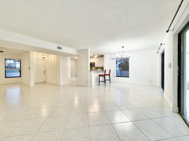 unfurnished room featuring light tile patterned floors, a textured ceiling, a chandelier, visible vents, and baseboards