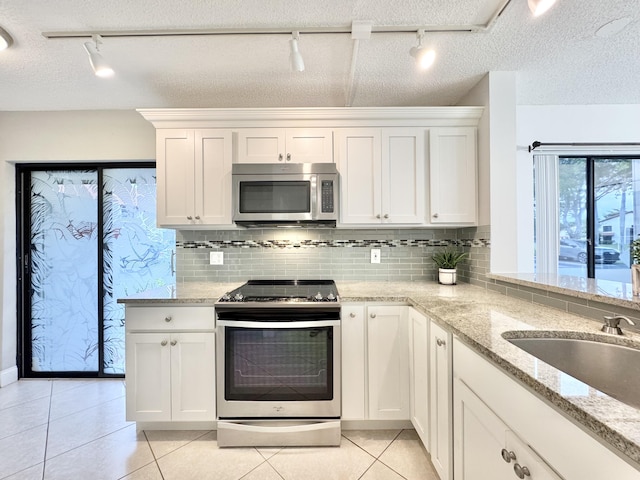 kitchen with light tile patterned flooring, a sink, white cabinetry, appliances with stainless steel finishes, and light stone countertops