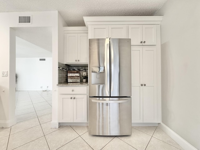 kitchen with tasteful backsplash, visible vents, white cabinets, light tile patterned flooring, and stainless steel fridge