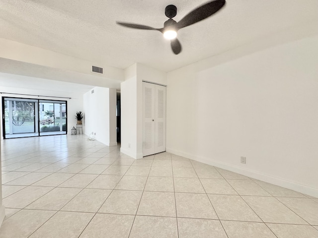 empty room featuring light tile patterned floors, a textured ceiling, visible vents, baseboards, and a ceiling fan