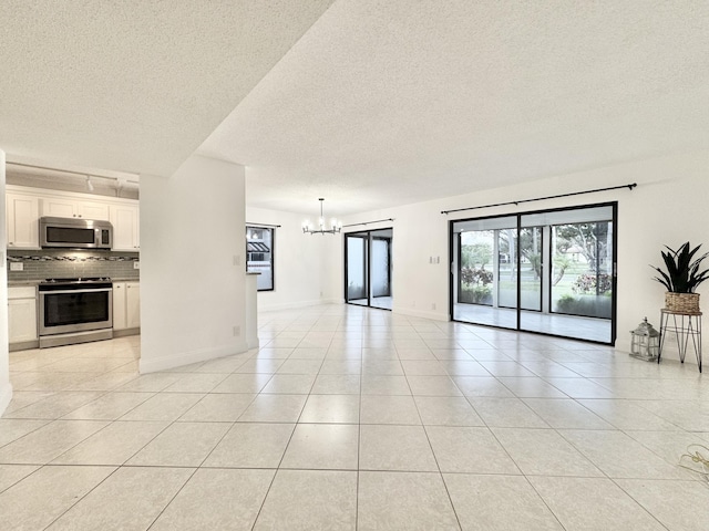 unfurnished living room featuring a notable chandelier, a textured ceiling, baseboards, and light tile patterned floors