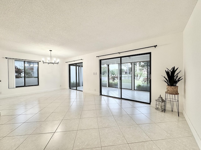 empty room featuring a chandelier, a textured ceiling, baseboards, and light tile patterned floors