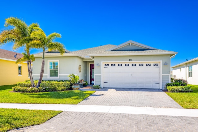 ranch-style home featuring a front yard, an attached garage, a shingled roof, stucco siding, and decorative driveway