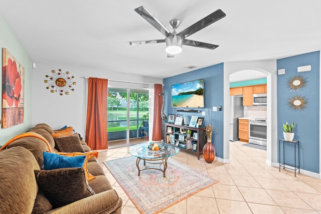 living area with light tile patterned floors, visible vents, arched walkways, baseboards, and a ceiling fan