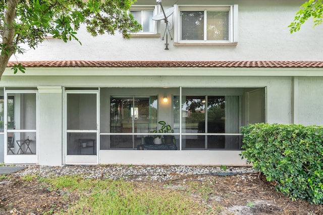 back of property featuring a tiled roof, a sunroom, and stucco siding