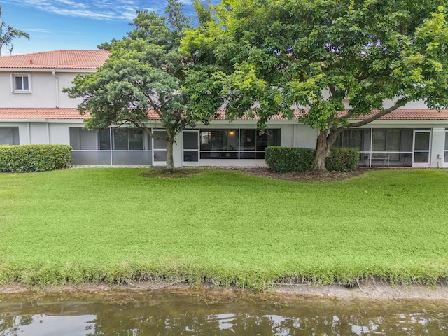 rear view of house with a lawn, a sunroom, a tile roof, a water view, and stucco siding