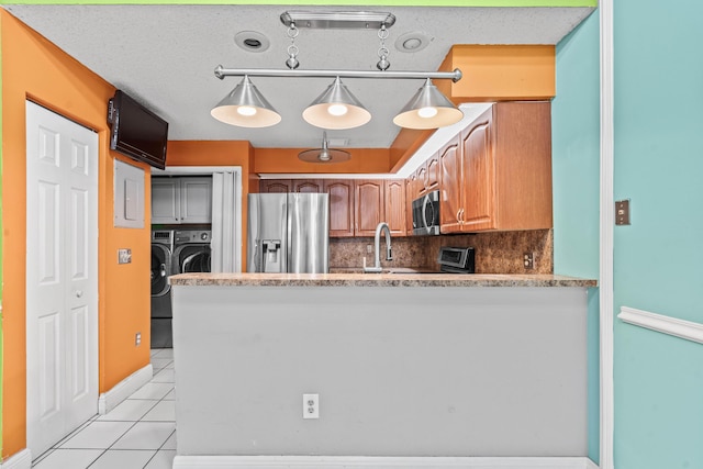 kitchen with light tile patterned flooring, a peninsula, separate washer and dryer, appliances with stainless steel finishes, and tasteful backsplash