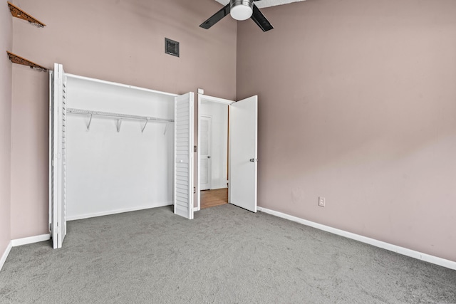 unfurnished bedroom featuring ceiling fan, a high ceiling, carpet flooring, visible vents, and baseboards