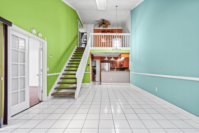 unfurnished living room with baseboards, ceiling fan, ornamental molding, tile patterned floors, and stairs