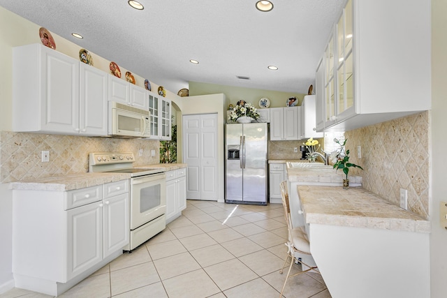 kitchen with lofted ceiling, white appliances, light tile patterned flooring, and white cabinets