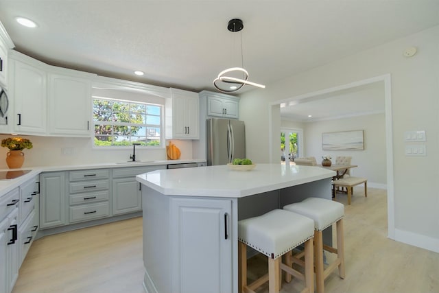 kitchen with a sink, a kitchen breakfast bar, light countertops, freestanding refrigerator, and a center island