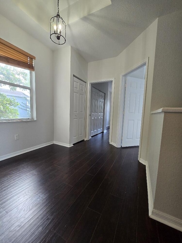 interior space with dark wood-style floors, a notable chandelier, a textured ceiling, and baseboards