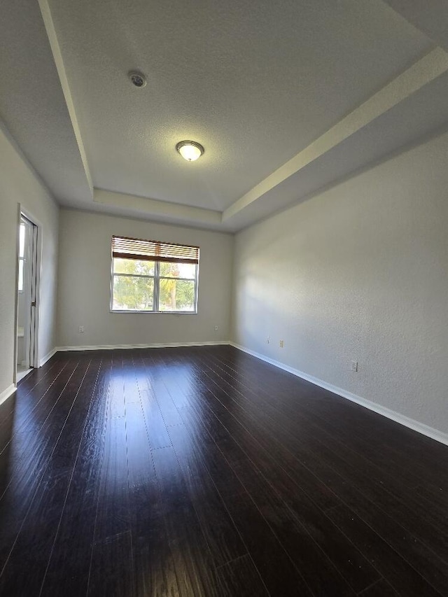 unfurnished room featuring dark wood-type flooring, a raised ceiling, a textured ceiling, and baseboards