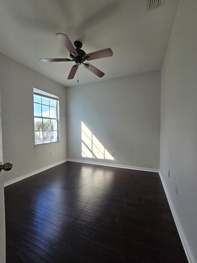 empty room with dark wood-style floors, visible vents, a ceiling fan, and baseboards