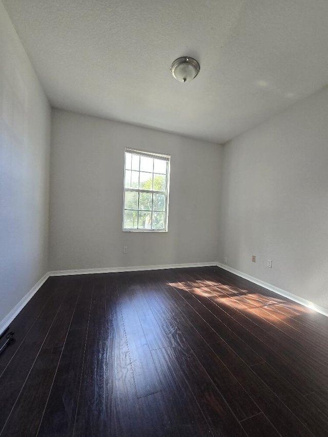 unfurnished room featuring a textured ceiling, dark wood-type flooring, and baseboards