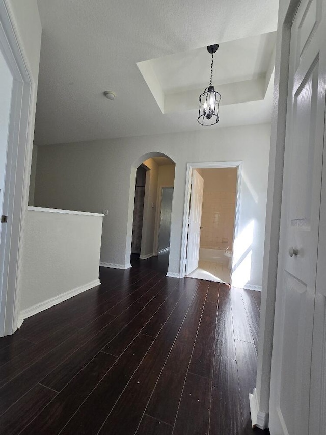 interior space featuring a tray ceiling, arched walkways, baseboards, and wood finished floors