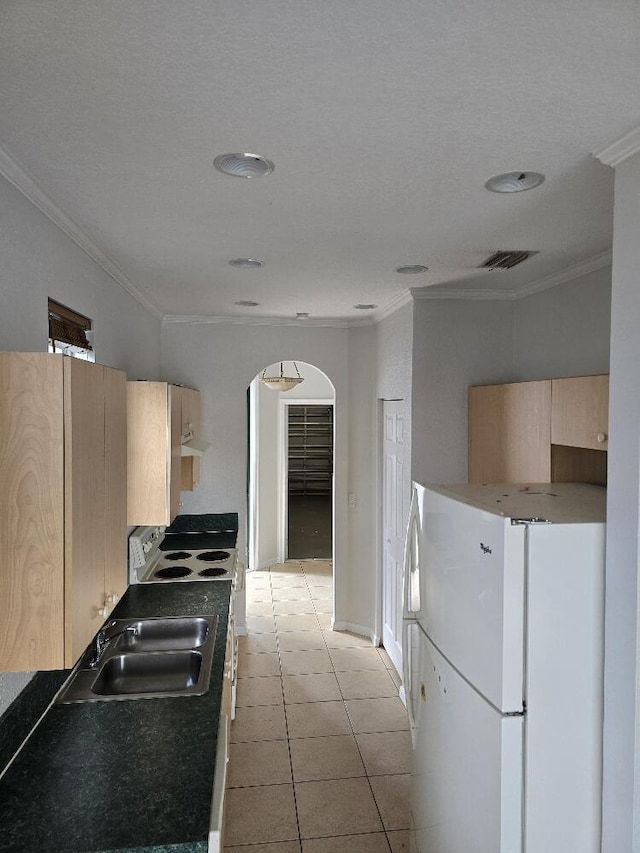 kitchen featuring arched walkways, light tile patterned floors, freestanding refrigerator, light brown cabinets, and a sink