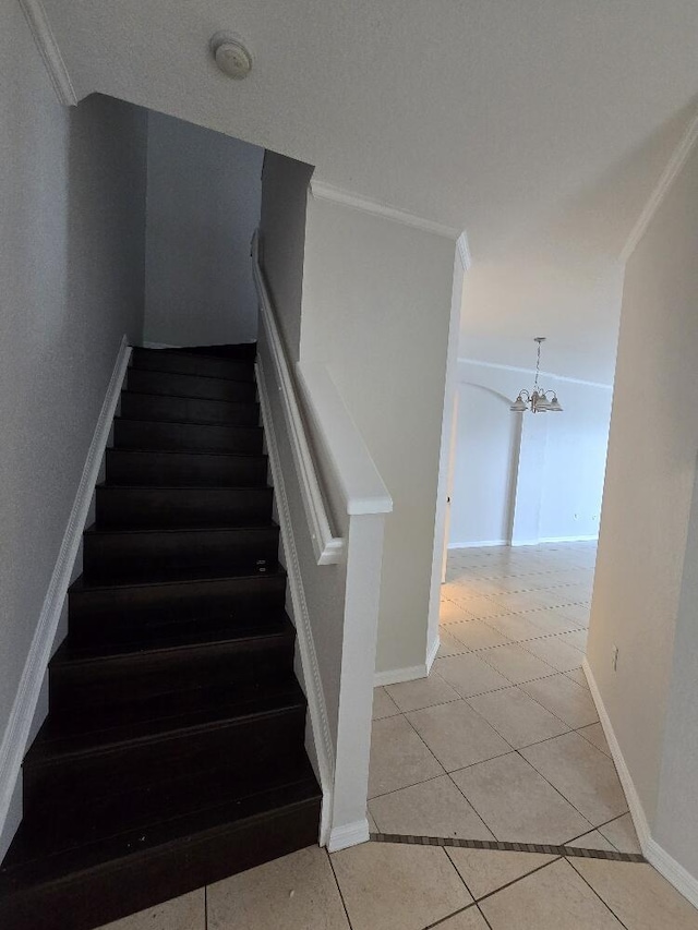 stairs featuring a chandelier, ornamental molding, baseboards, and tile patterned floors