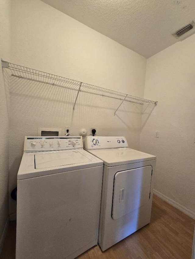 laundry area with laundry area, visible vents, wood finished floors, a textured ceiling, and separate washer and dryer