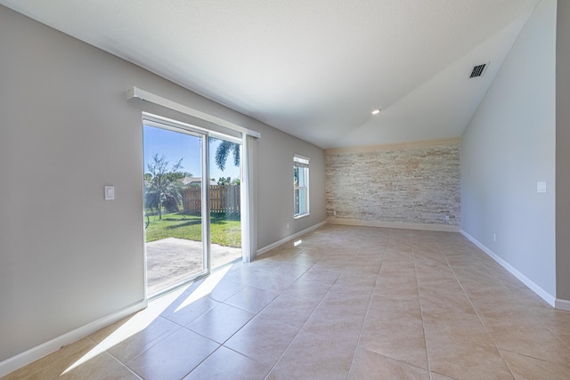 empty room featuring lofted ceiling, light tile patterned floors, and baseboards