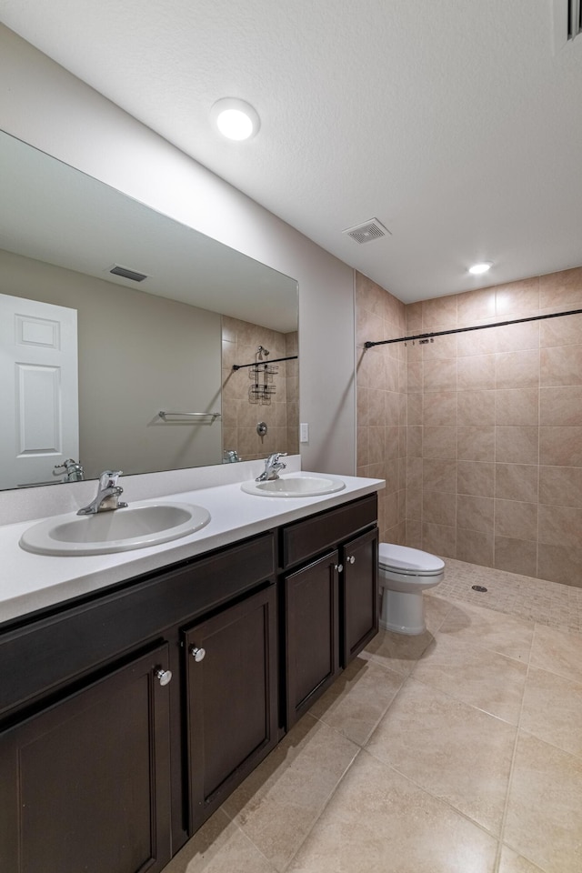 bathroom with a tile shower, double vanity, a sink, and toilet