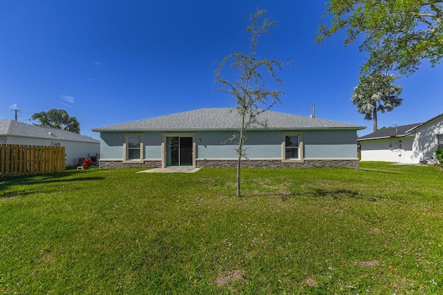 rear view of house with stone siding, a lawn, fence, and stucco siding