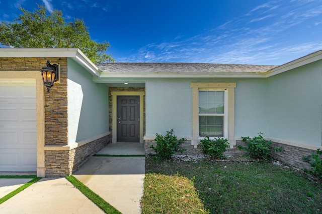 entrance to property featuring a garage, stone siding, roof with shingles, and stucco siding